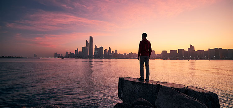 person on rocky shore looking at city across the water