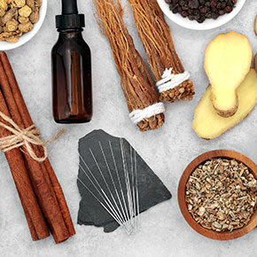 bundles of herbs and bottle with dropper and acupuncture needles arranged on table
