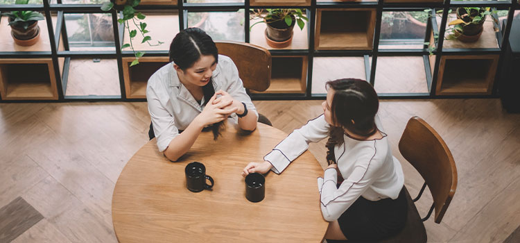two professionals talking at table with coffee mugs