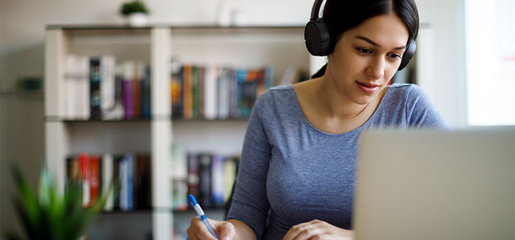 woman with headphones on taking notes from laptop