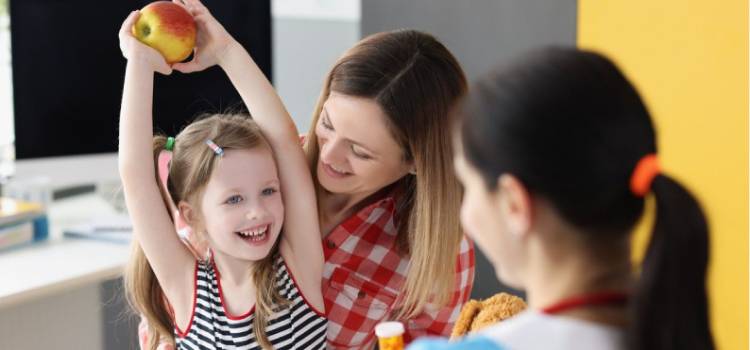 young-girl-holding-an-apple-above-her-head-and-smiling-at-a-pediatric-nutritionist