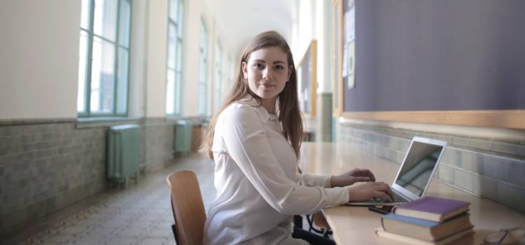 brown haired female studying for exam on laptop facing camera with subtle smile