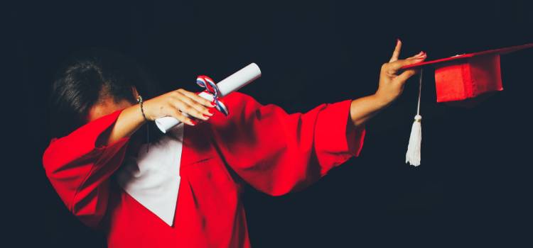 graduate in a red gown diploma in one hand and hat in other