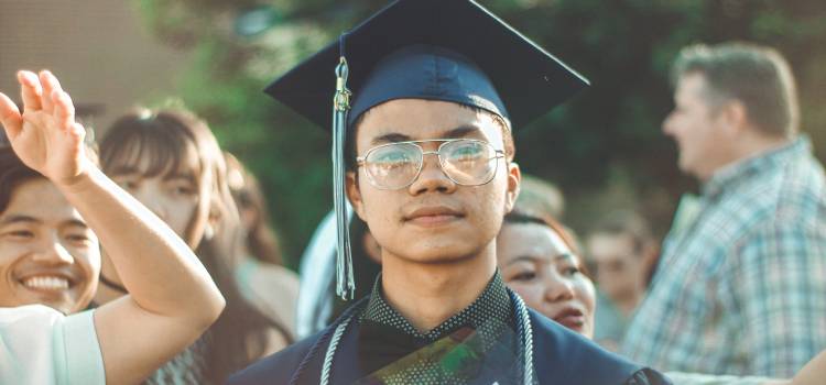 graduate of kinesiology masters program with cap and glasses looking proudly at camera