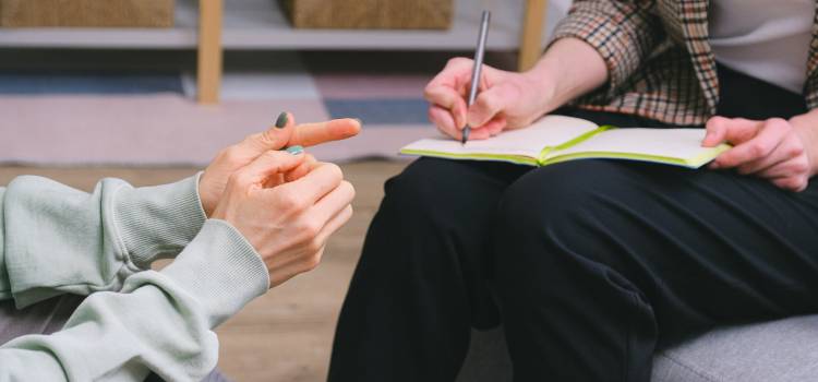 two people sitting one of them writing notes in an open notebook