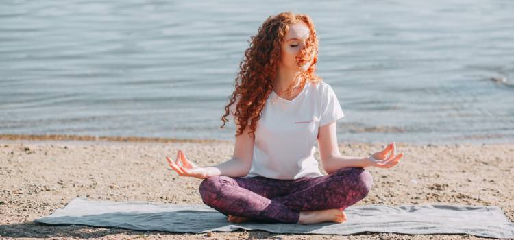woman with curly red hair meditating on the beach