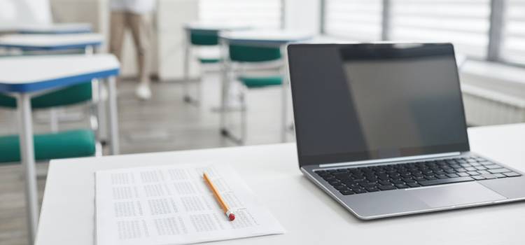 pencil and paper exam on a white desk next to an open laptop