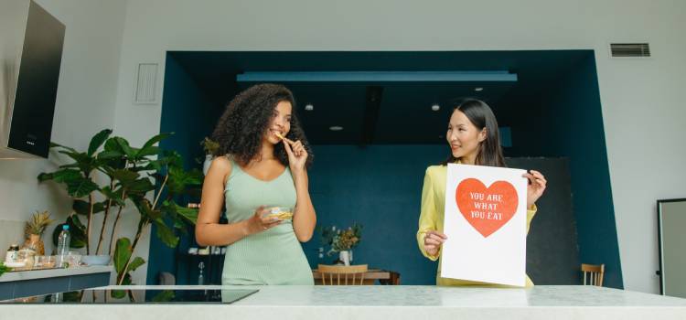 nutritionist holding a book as her smiling colleague takes a bite of food