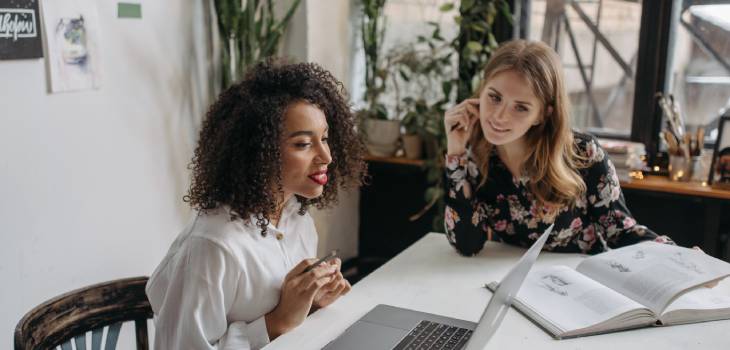 two female holistic health students staring at an open book and a laptop