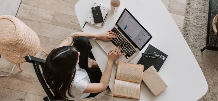 woman sitting at desk with her laptop and open books to the side