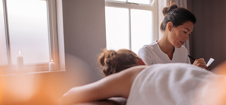 female massage therapist takes notes on new client before massage
