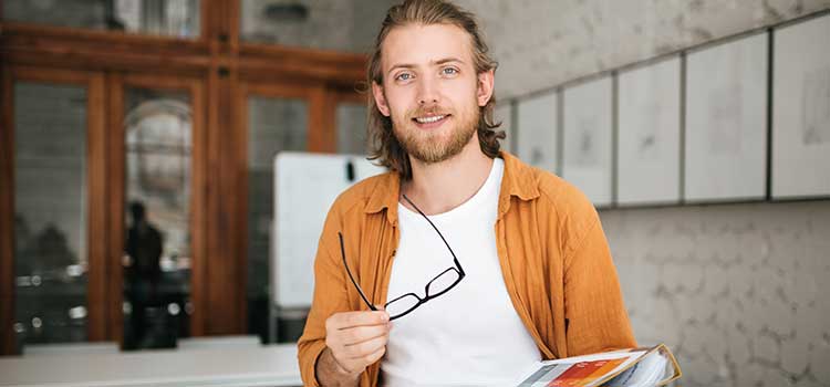 male college student holds glasses and notebook at university door