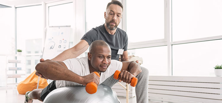 physical therapist helps client stay balanced on pt ball