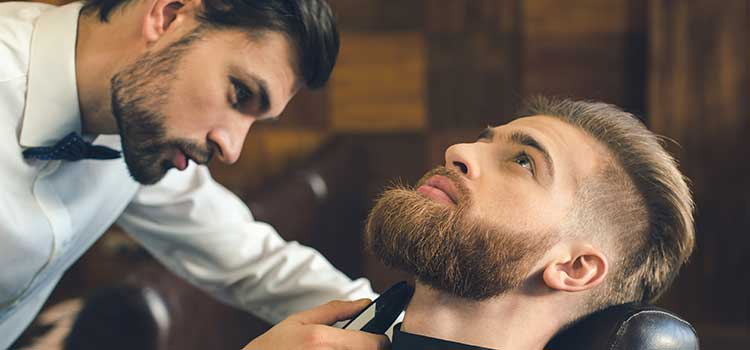 male cosmetologist trims clients beard