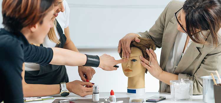 student at cosmetology school gets advice from instructor on makeup technique