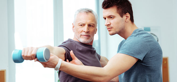 physical therapist helps senior hold weight for shoulder rehab