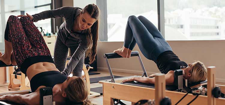pilates instructor corrects student alignment during pilates class