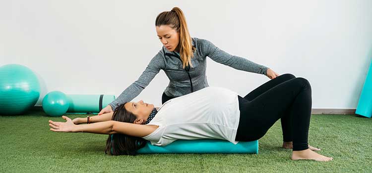 physical therapist works with pregnant woman on floor mat
