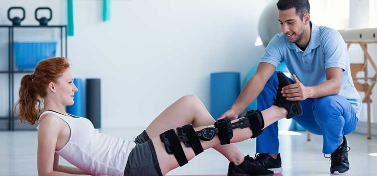 physical therapist helps woman with leg brace stretch