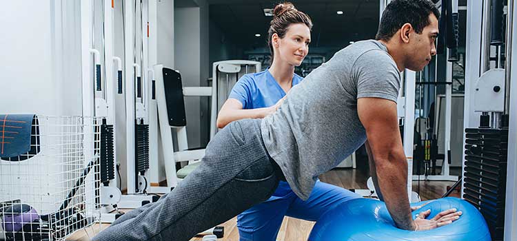 female pt helps man do prone exercise on medicine ball