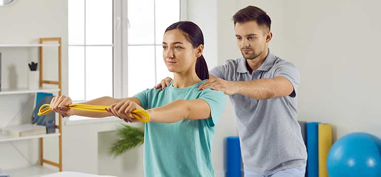 physical therapist helps client keep shouulders aligned while she stretches with band