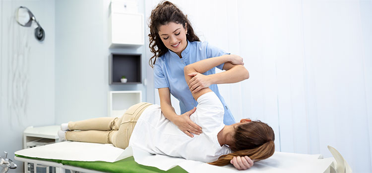smiling chiropractor aligns prone patients shoulder blade